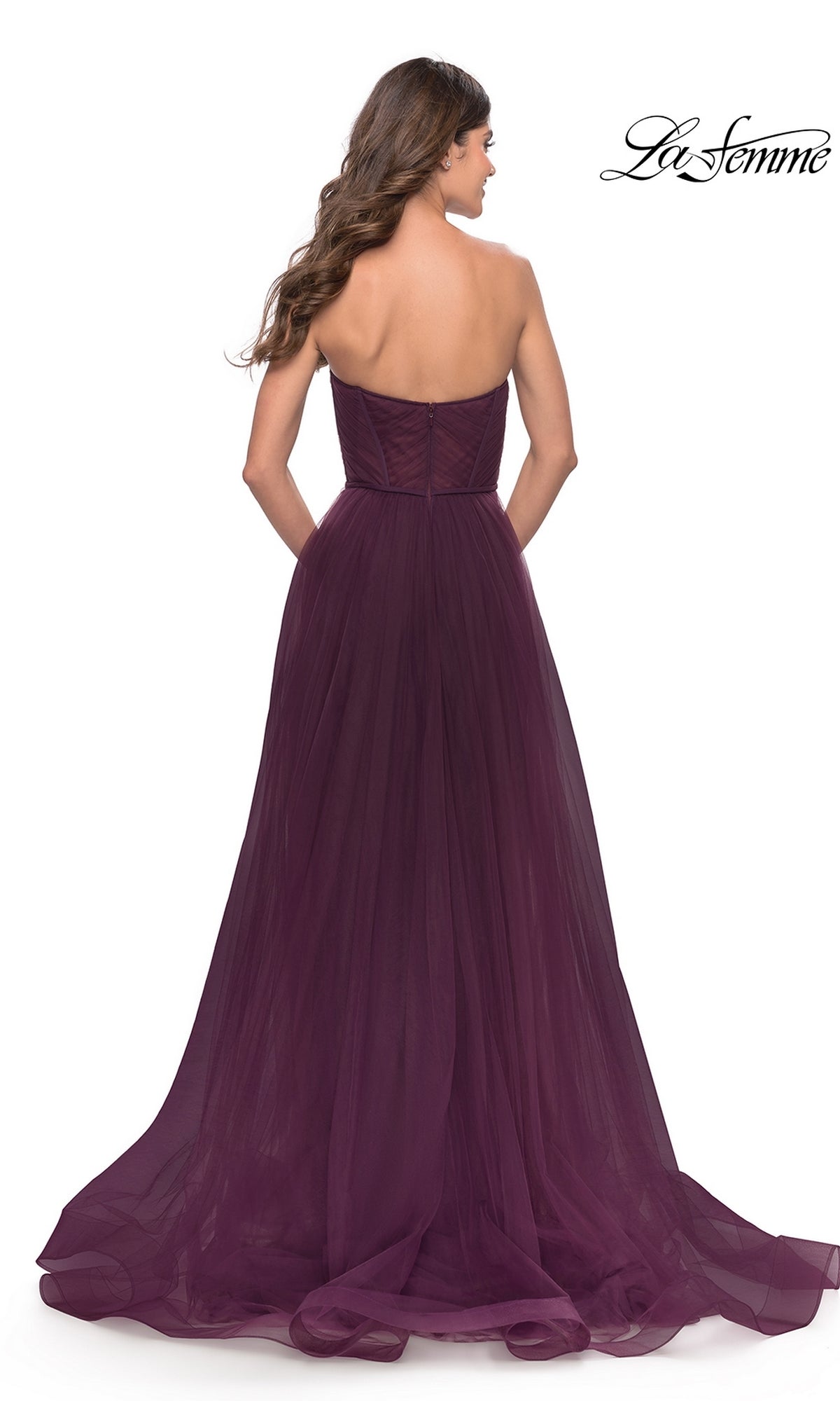 A woman faces away in the Strapless Long Prom Ball Gown: La Femme 31205, a floor-length dark purple A-line dress with tulle skirt, slight train, and flattering fitted bodice. The La Femme logo appears in the corner.